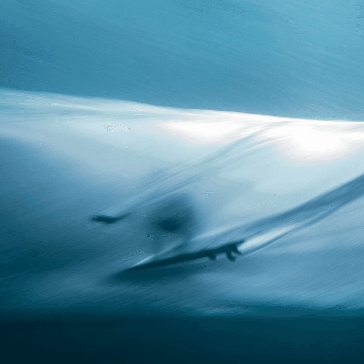 A long exposure blur of a surfer inside a breaking wave, in deep blue tones.