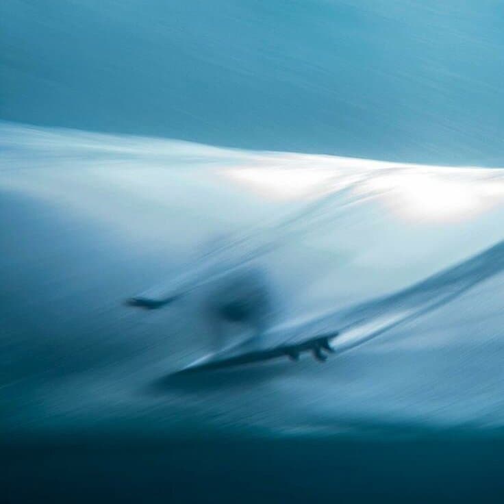 A long exposure blur of a surfer inside a breaking wave, in deep blue tones.